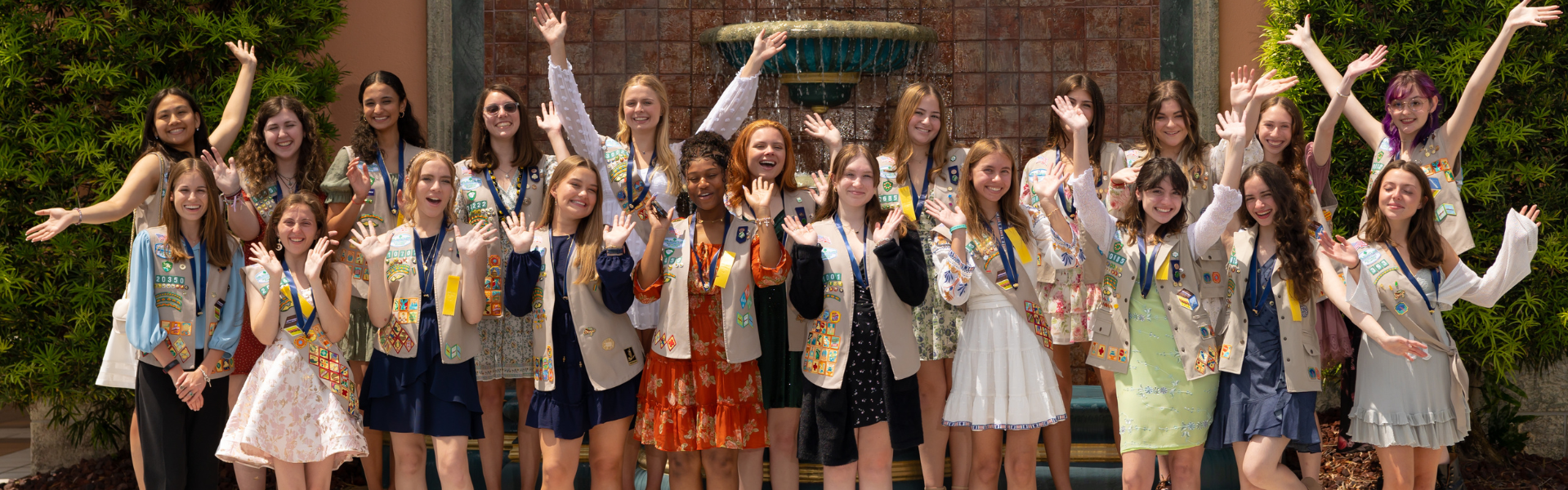  Group of kindergarten daisy girl scouts in vest and apron uniform hugging and smiling outside. 