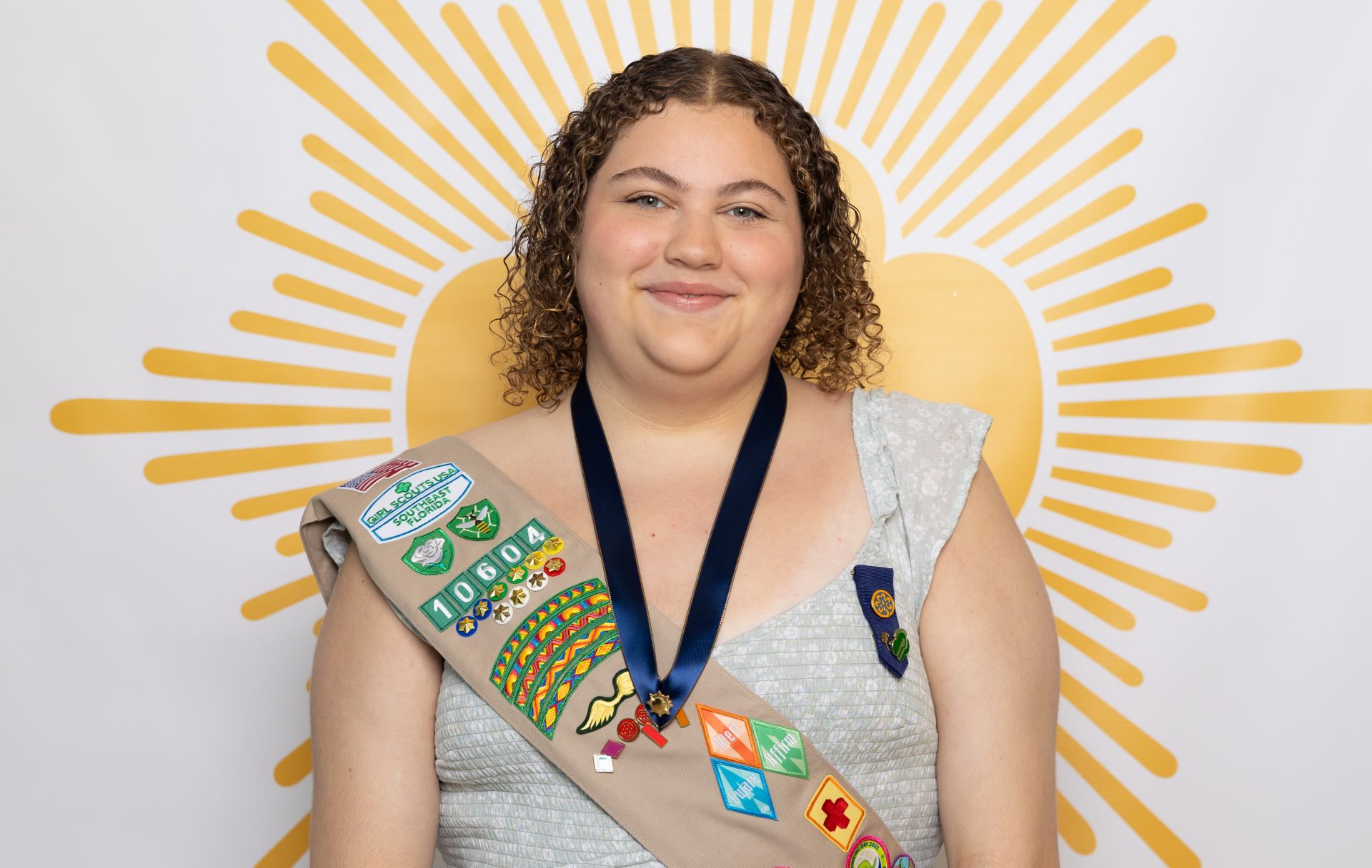 ambassador high school girl scout wearing sash outside against green background